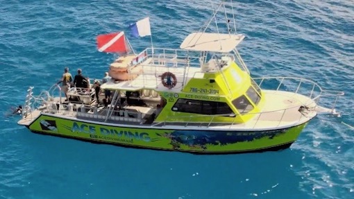 A professional dive boat is anchored off the coast of Miami Beach with crew and divers in water for a scuba diving experience.
