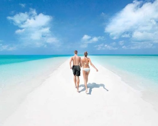 Beach couple stroll Bahamas Sandbar A couple stroll hand in hand along a Bahamas beach with the blue ocean on both sides and among blue skies.