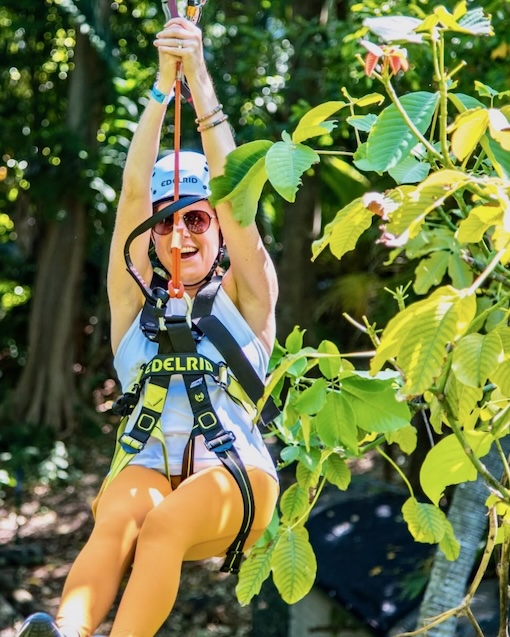 Girl zips across a line in the treetops of Miami during a trekking adventure.