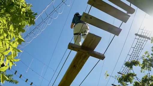 A man walks across a tight rope during treetop trekking obstacle course in Miami